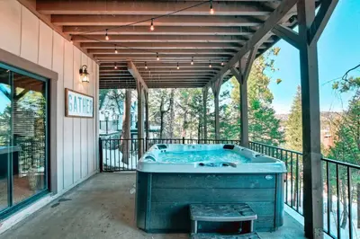 an outdoor hot tub on a patio with a deck at Stunning LAKE VIEW Game Room Spa Walk To Village in Lake Arrowhead