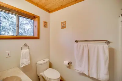 a white bathroom with a toilet and a window at Peaceful and Idyllic Forest Cabin with Pool Table in Pine Mountain Club