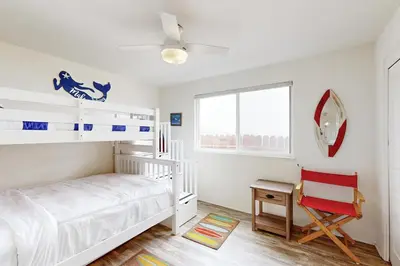 a white bedroom with a bunk bed and a red chair at Brink of Paradise in Carpinteria