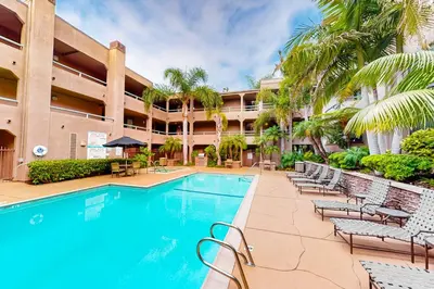 a swimming pool in front of a hotel with chairs and palm trees at Pacific Cove Unit 111 in Los Angeles