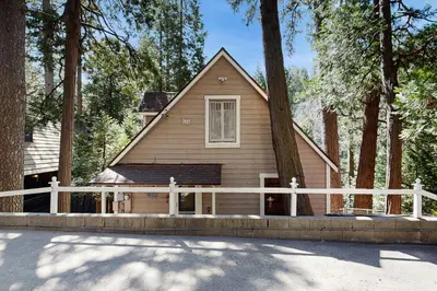 a small house with a white fence and trees at The Cottage in Lake Arrowhead