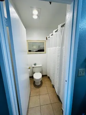 a bathroom with a toilet and white shower curtain at Casa Blanca Hotel - Cypress, Buena Park in Cypress
