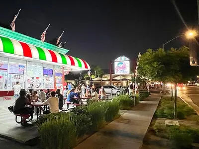 people sitting at tables outside a restaurant at night at Bposhtels Anaheim in Anaheim