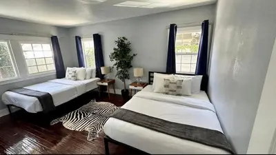 two beds in a room with two windows at Hollywood house with parking - walk to attractions in Los Angeles