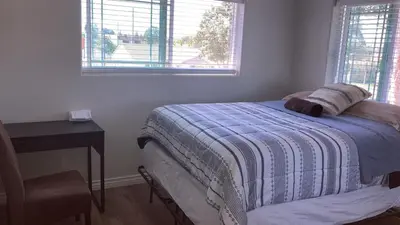a bedroom with a bed and a table and two windows at We are in this together in Santa Ana