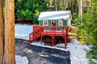 a small green and red house in the woods at Running Springs Cabin with Deck and Forest Views in Running Springs