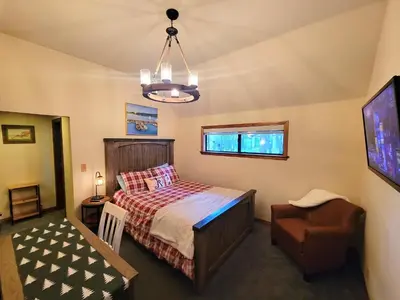a bedroom with a bed and a chair and a tv at Four Seasons Getaway-Private Hot Spa with Pine Tree Views-Walk to Village and Pineknot Trailhead-Plus King Bed! in Big Bear Lake