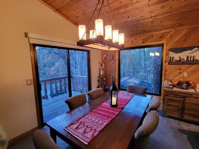 a dining room with a table and two large windows at Four Seasons Getaway-Private Hot Spa with Pine Tree Views-Walk to Village and Pineknot Trailhead-Plus King Bed! in Big Bear Lake