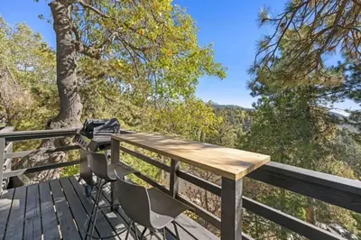 a wooden table and chairs on a deck with trees at Updated Mountain Cabin Retreat with 180 views off Deck and Balcony in Running Springs