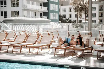 two women laying on lounge chairs next to a swimming pool at Level Long Beach - East Village in Long Beach