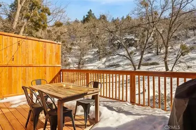 a wooden table and chairs on a deck in the snow at Le Chalet of Arrowbear Lake in Running Springs